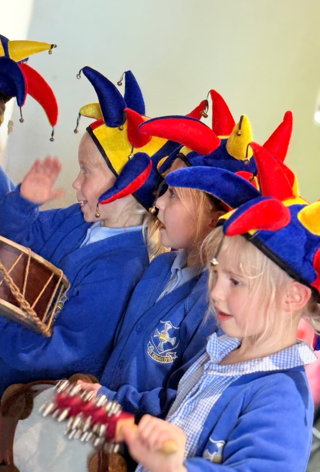 Three young children wear colorful jester hats while playing musical instruments.