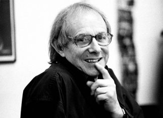 Portrait of Ken Loach smiling and pointing to his mouth